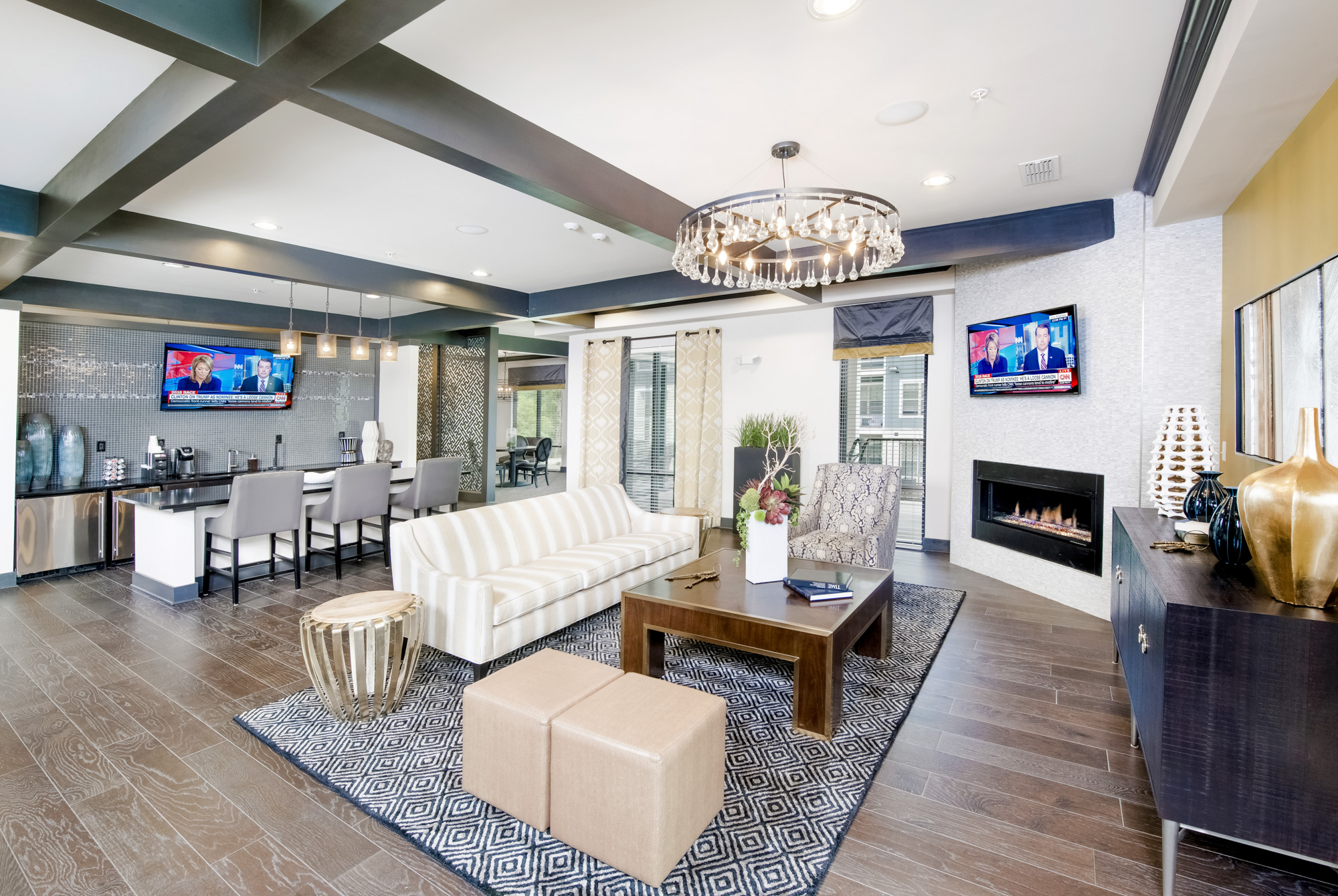 A seating area with a fireplace and mounted television on the right-side of the room with barstools surrounding a kitchen island and mounted television on the left.