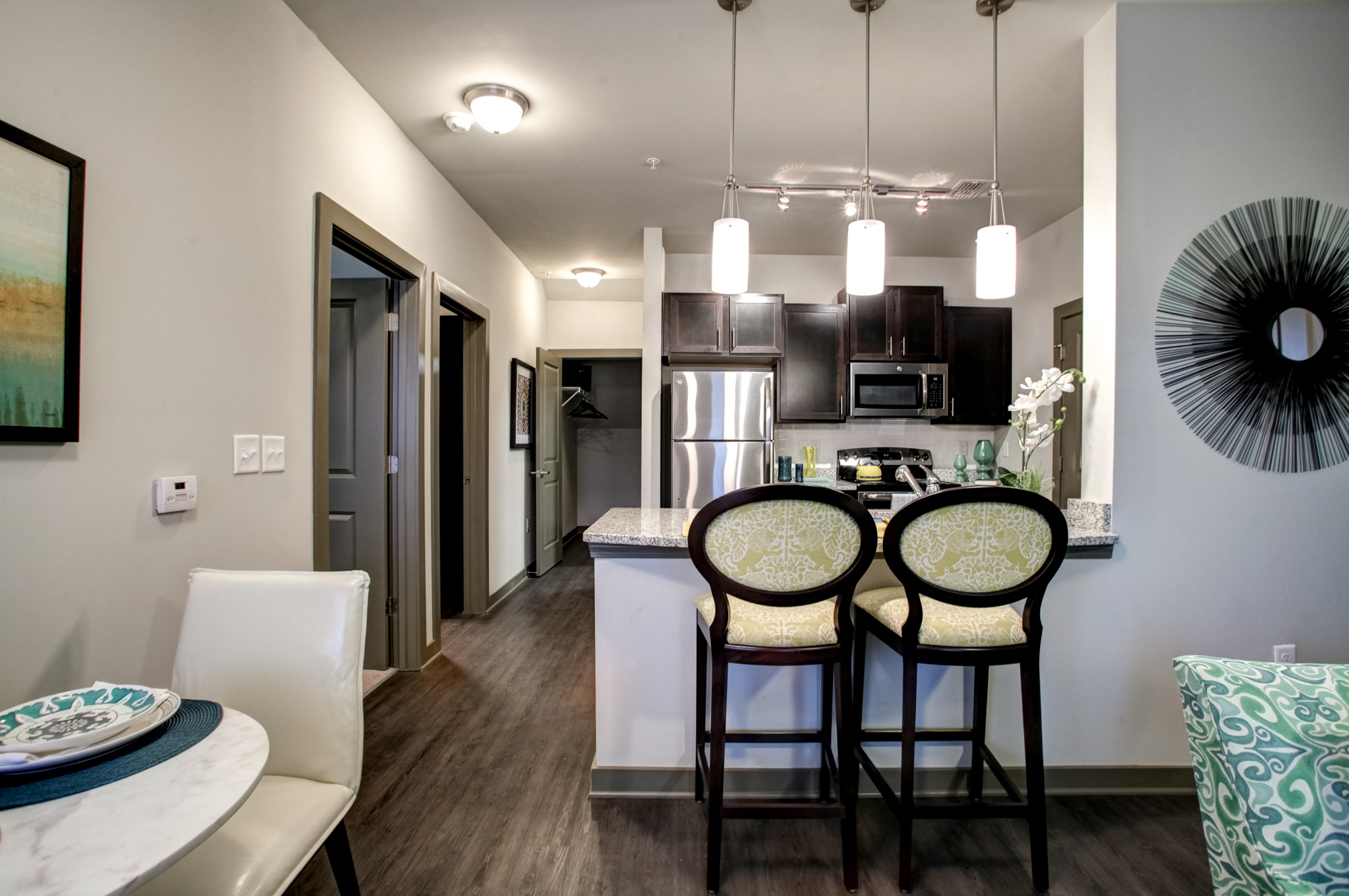 Two bar stools sit across from a kitchen with pendant lighting and stainless steel appliances.
