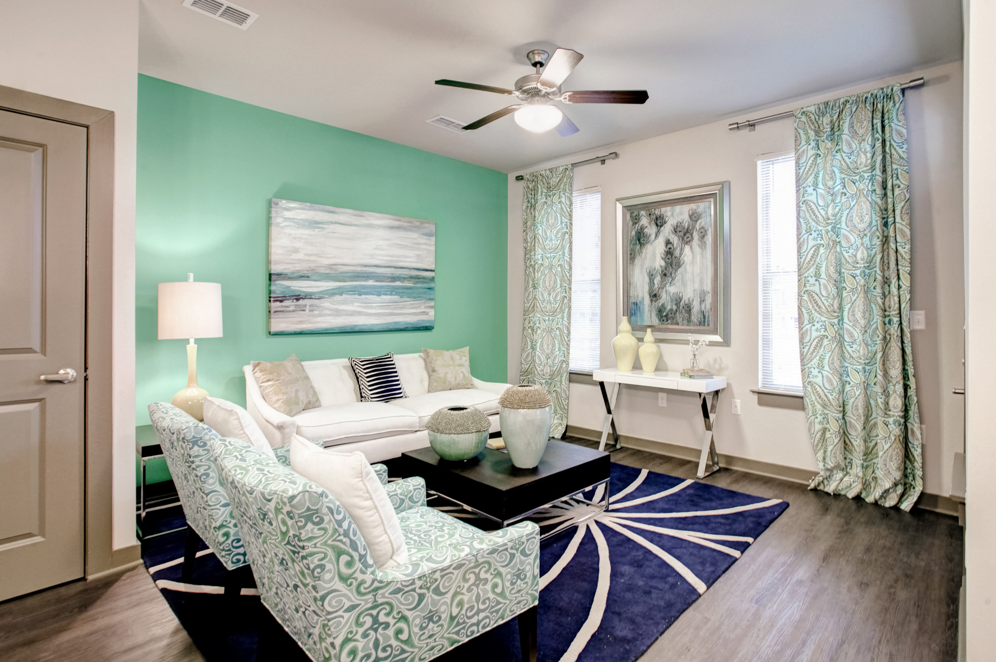 A mint green wall in the background with a white couch and brightly printed chairs at Park 9 apartments.