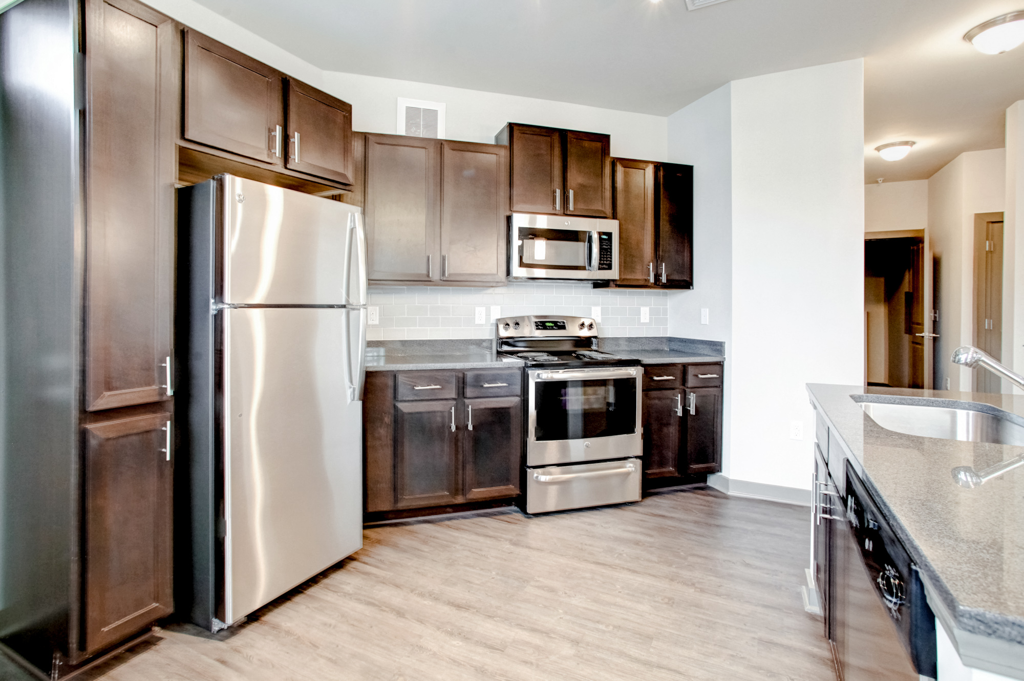 Stainless steel appliances sit inside a wood cabinets with wood-plank flooring on the ground.