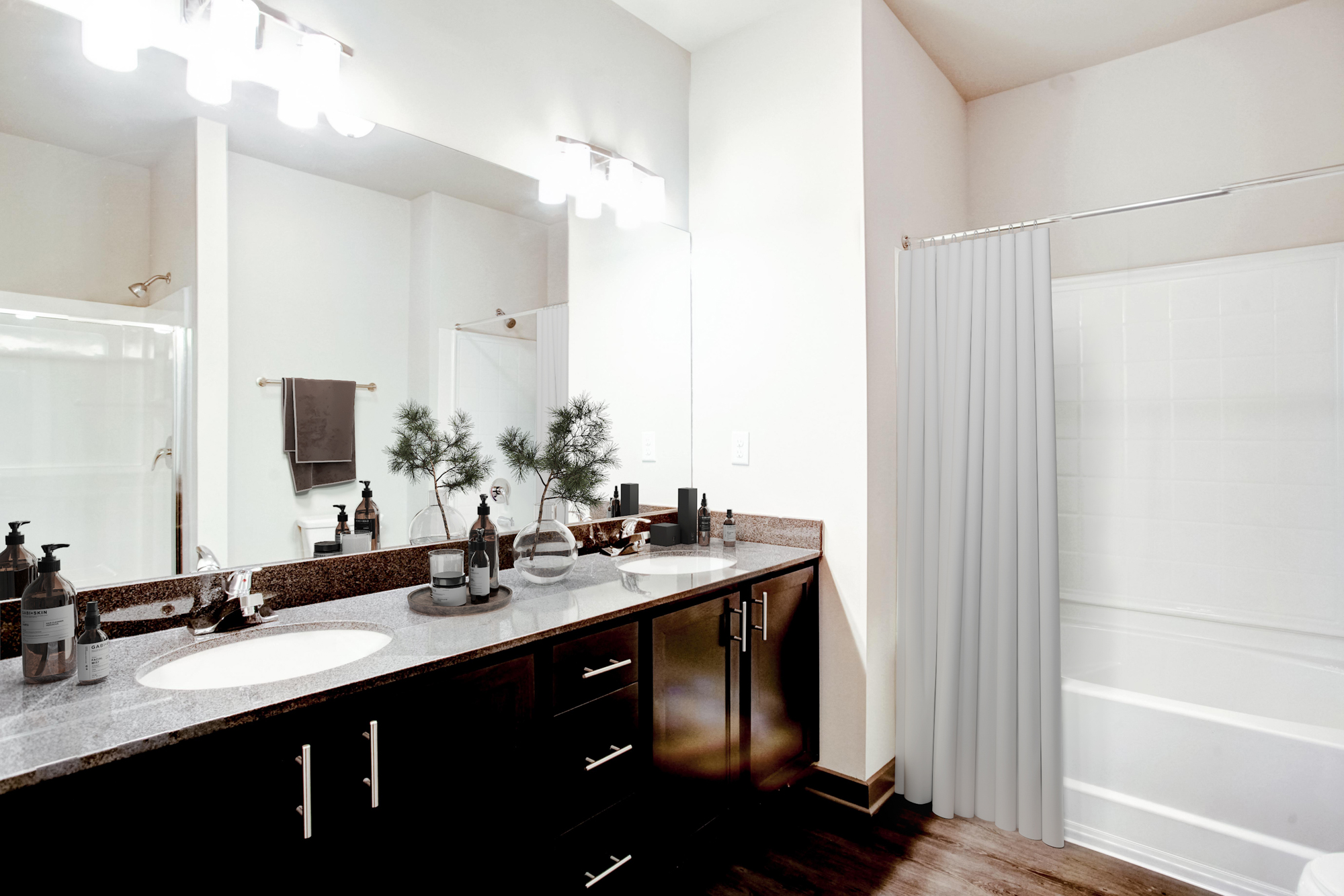 Double vanities sit atop brown colored cabinets with a dual shower and bath tub in the background.